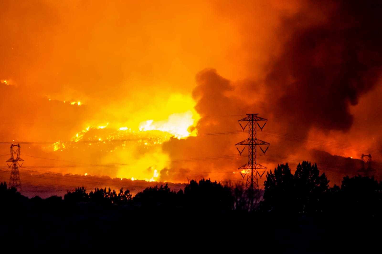 Wildfire glow behind transmission towers at night